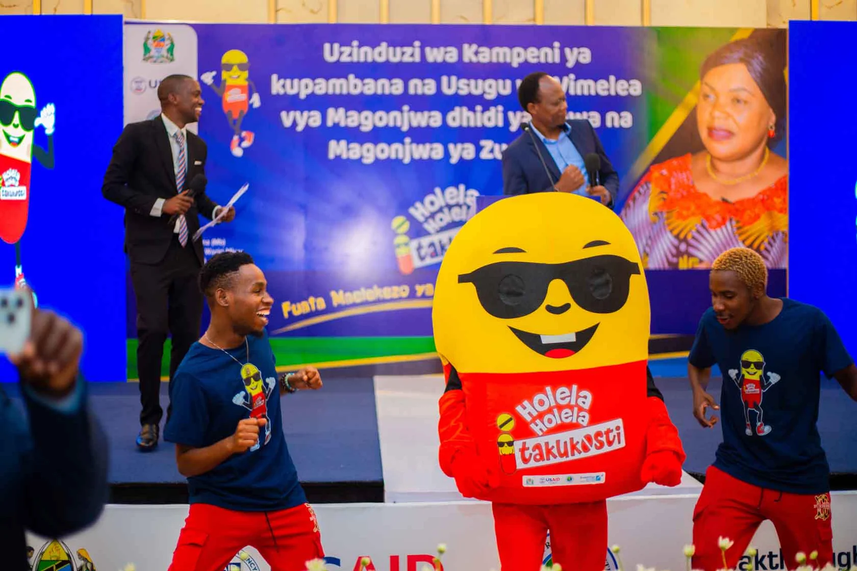 The Holela Holela mascot performing with dancers at a campaign launch